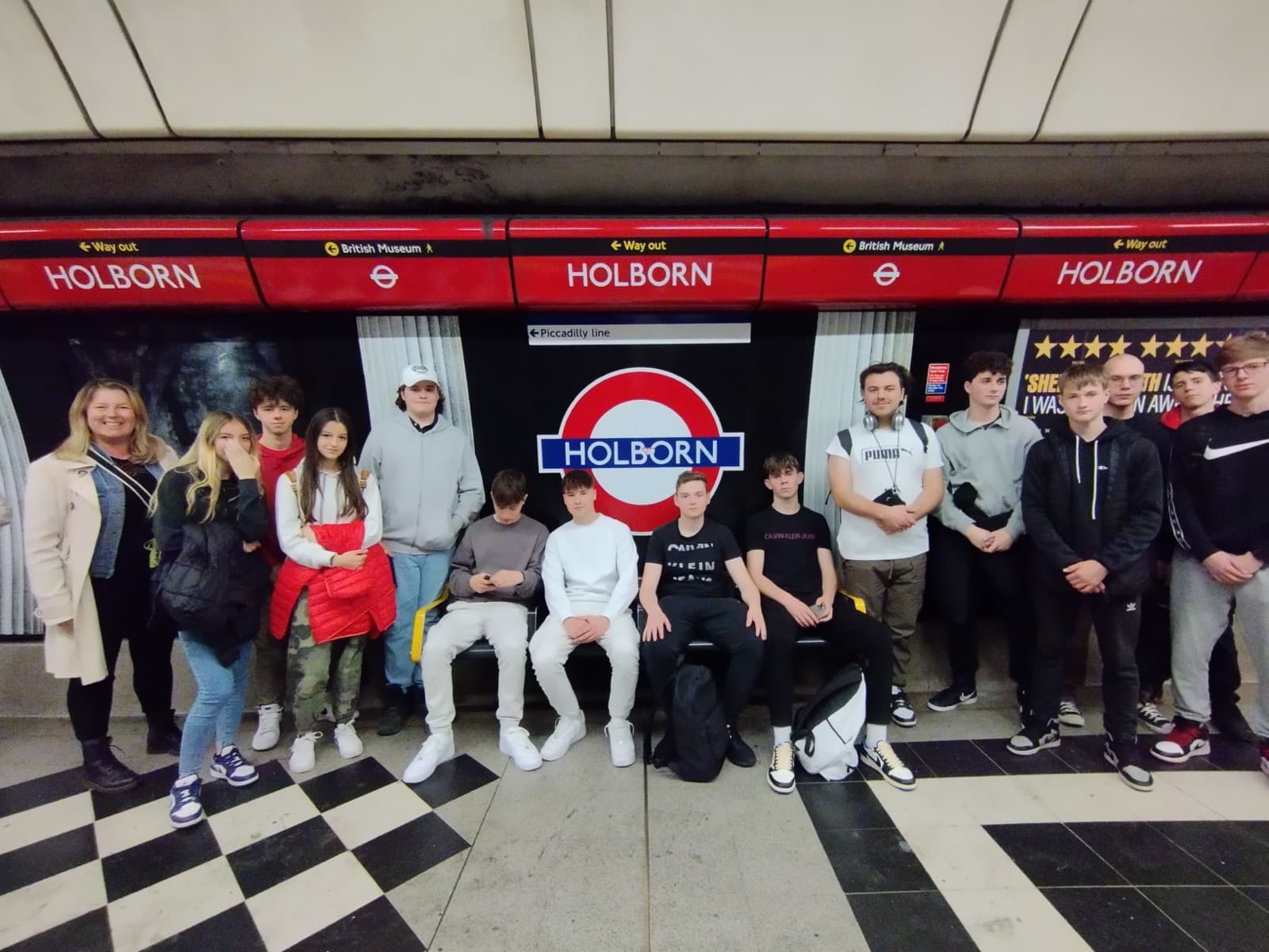 Dijaki slikani na podzemni postaji sedijo na klopi pred napisom HOLBORN