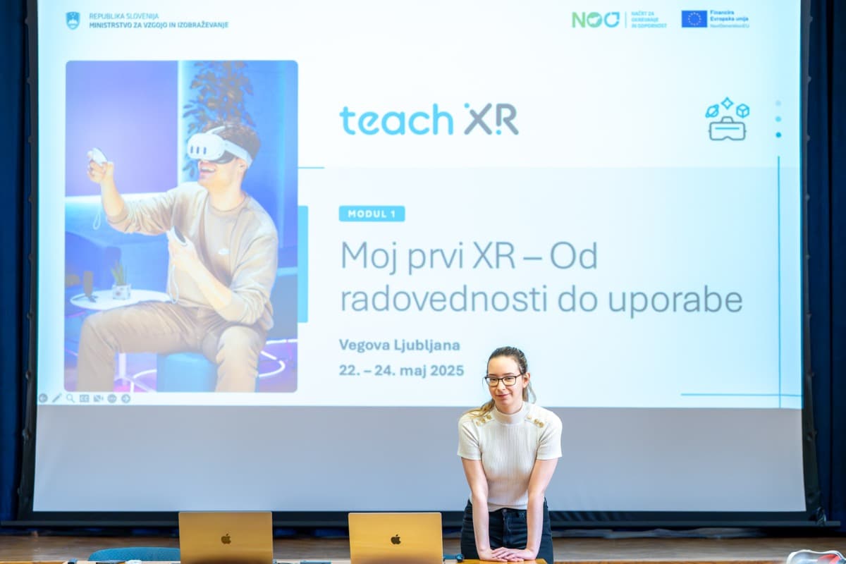 Predavateljica stoji pred platnom, na katerem je napisano Moj prvi XR – od radovednosti do uporabe.