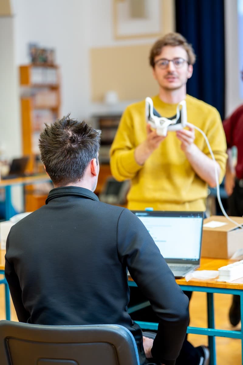 Predavatelj stoji pred udeležencem, v roki drži XR očala.