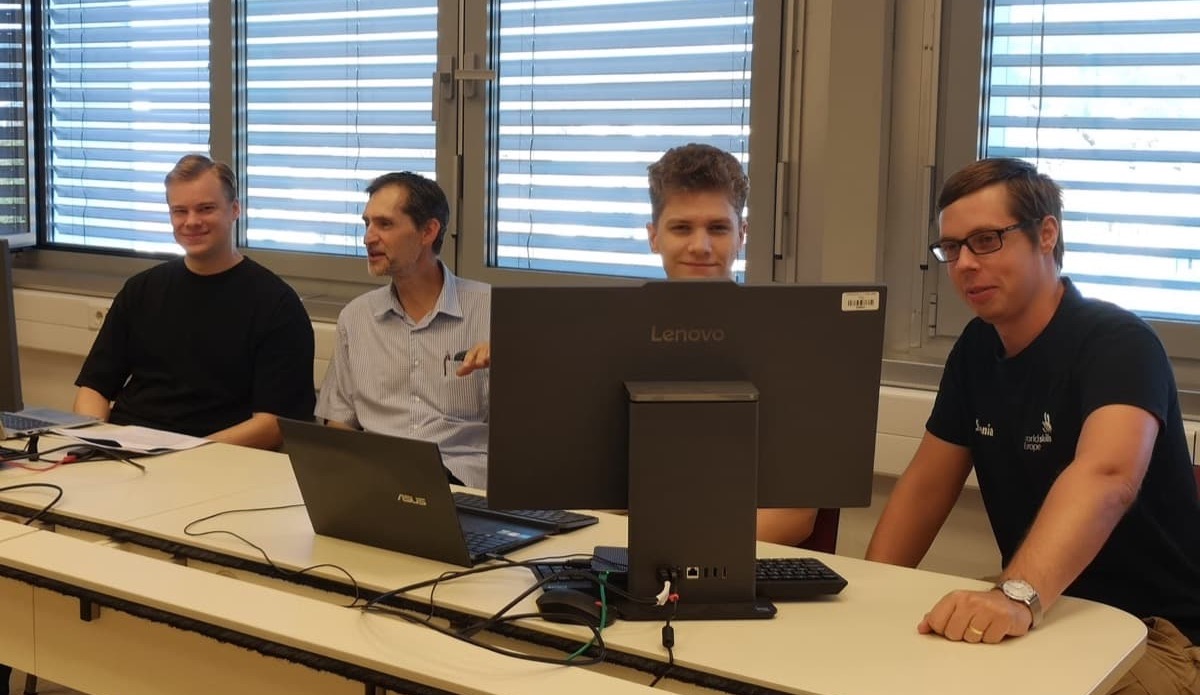 dijaka z mentorjema sedijo za računalniškim monitorjem