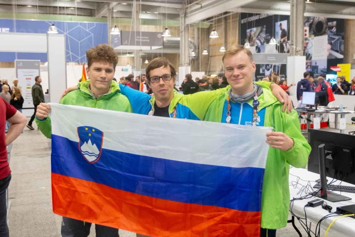 trije nasmejani tekmovalci Vegove z razprto slovensko zastavo.