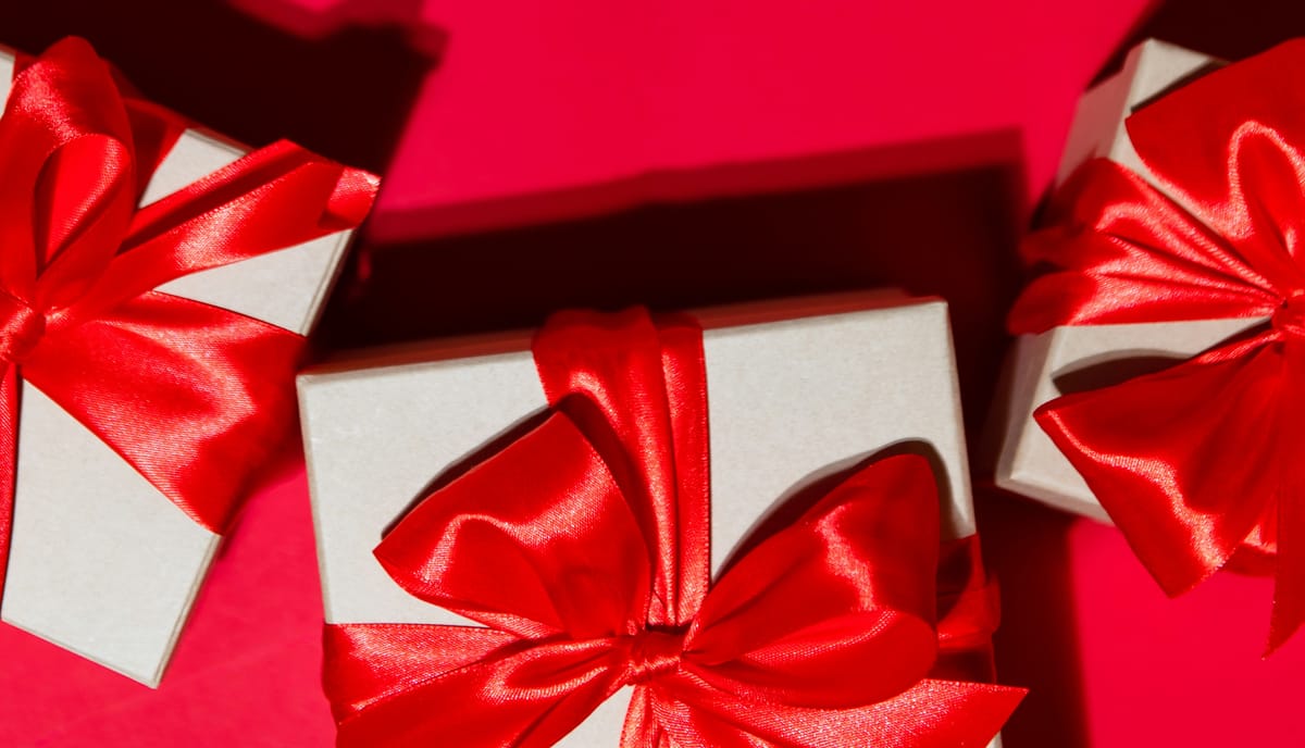 trije darilni paketi oviti z veliko rdečo mašno na rdeči podlagi