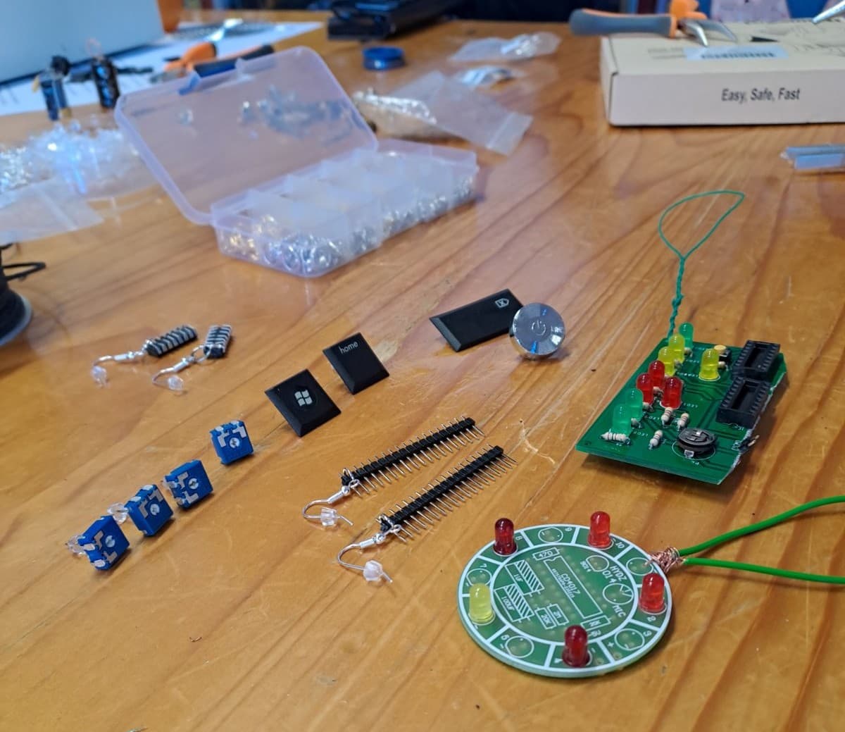 Kreativna delavnica v šolski knjižnici. Na mizi so iz e-odpadkov izdelani obeski, uhani in broške, orodje in deli za oblikovanje nakita.