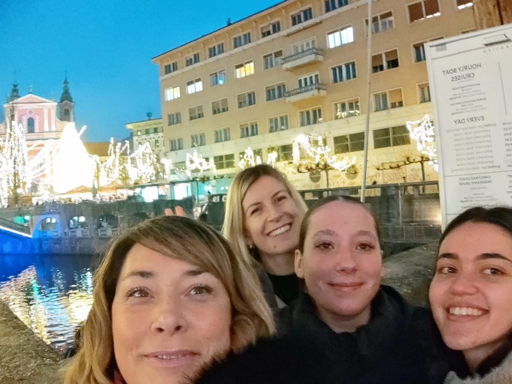 Dijakinji in profesorici na obrežju Ljubljanice, z lučkami v ozadju.