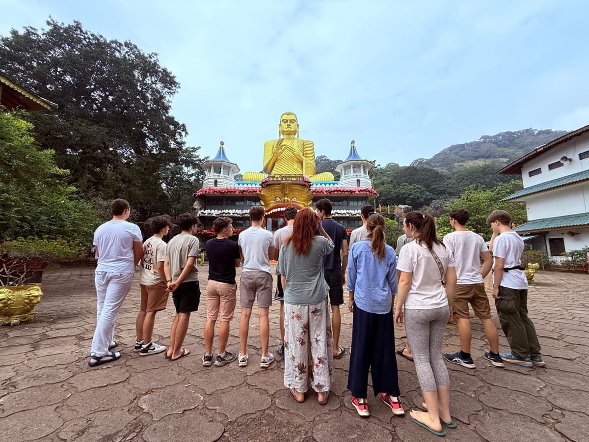 Dijaki stojijo pred templjem Zlatega Bude in opazujejo kip ter okrasje.