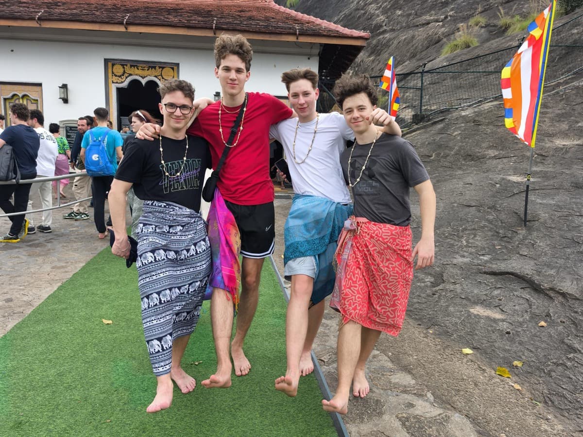 Dijaki bosi in oviti v krila stojijo pred jamskim templjem Dambulla.