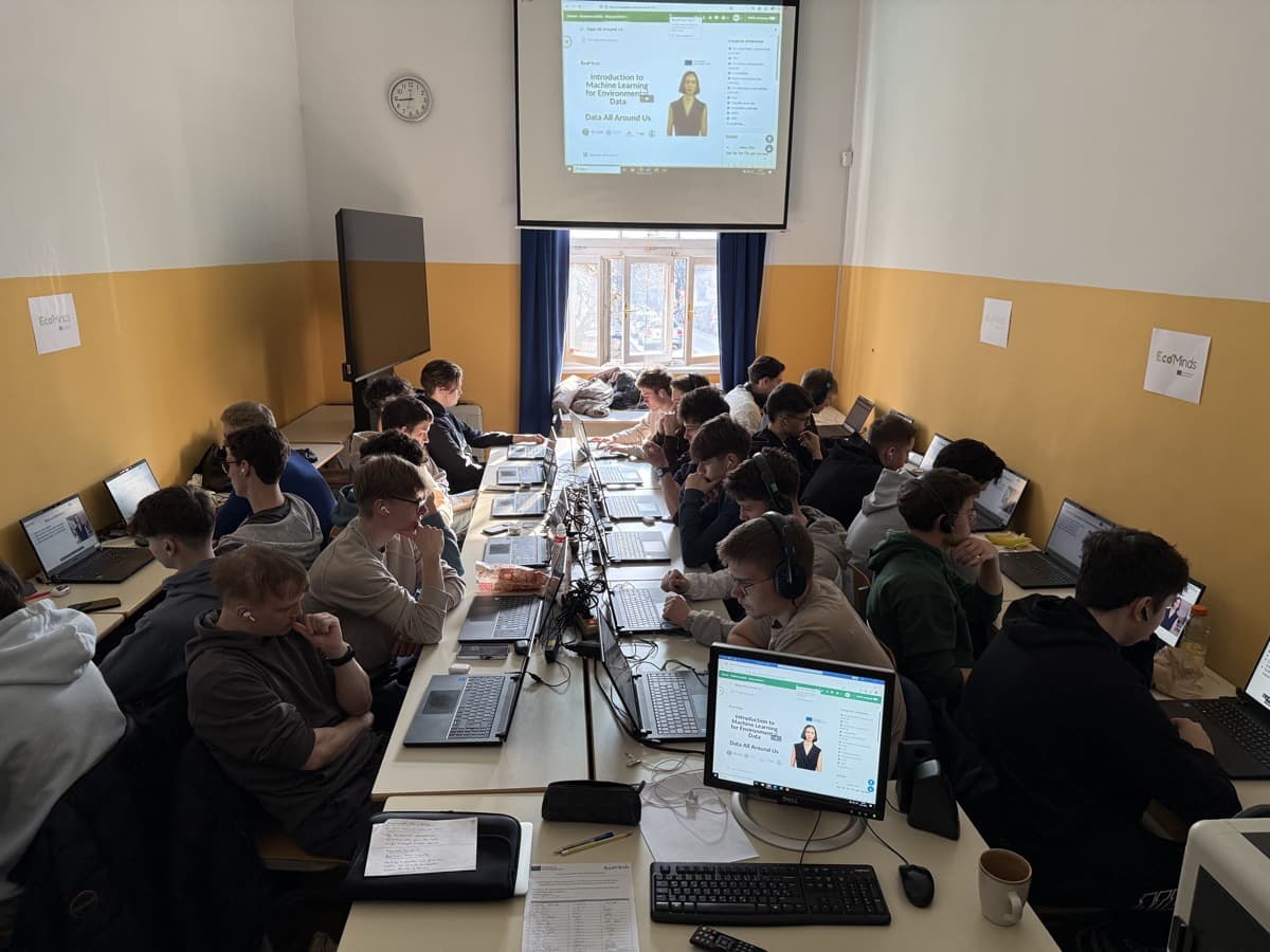 20 dijakov v učilnici sedijo drug ob drugem pred prenosniki in spremljajo seminar. V ozadju filmsko platno s prikazamo vsebine seminarja