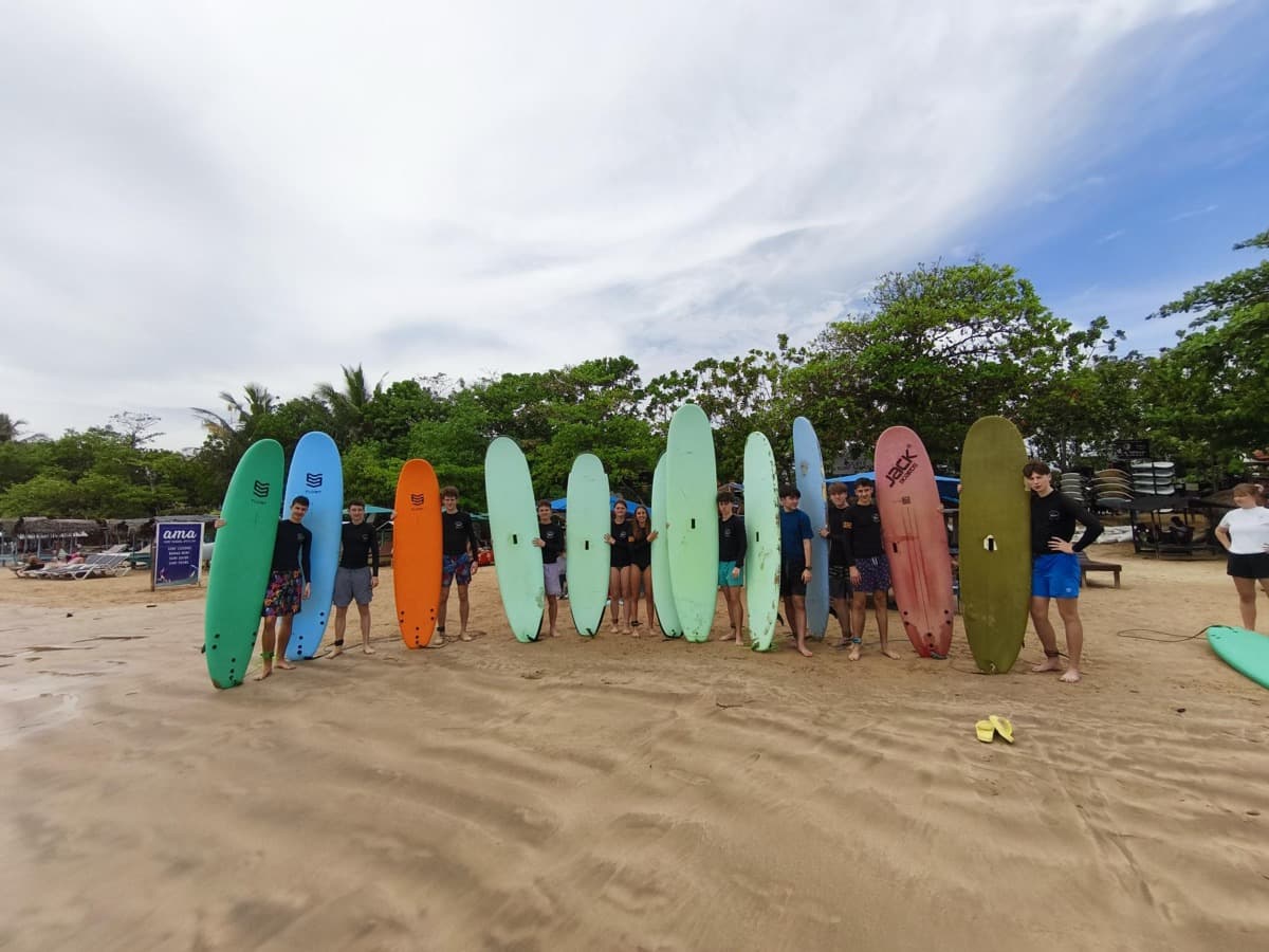 Dijaki z deskami stojijo na peščeni plaži in se pripravljajo na vstop v morje.