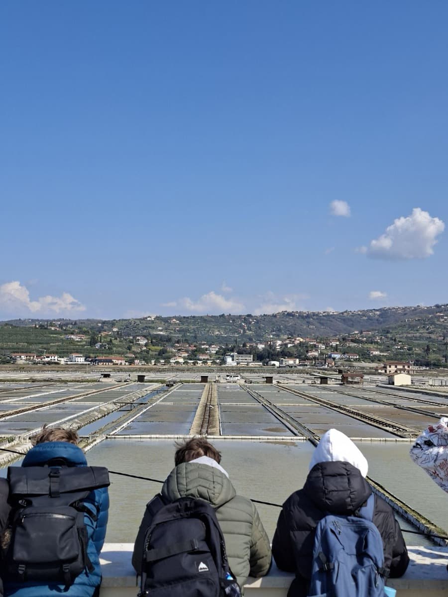 Trije sedeči dijaki, obrnjeni s hrbtom proti kameri, opazujejo solinske bazene pred sabo