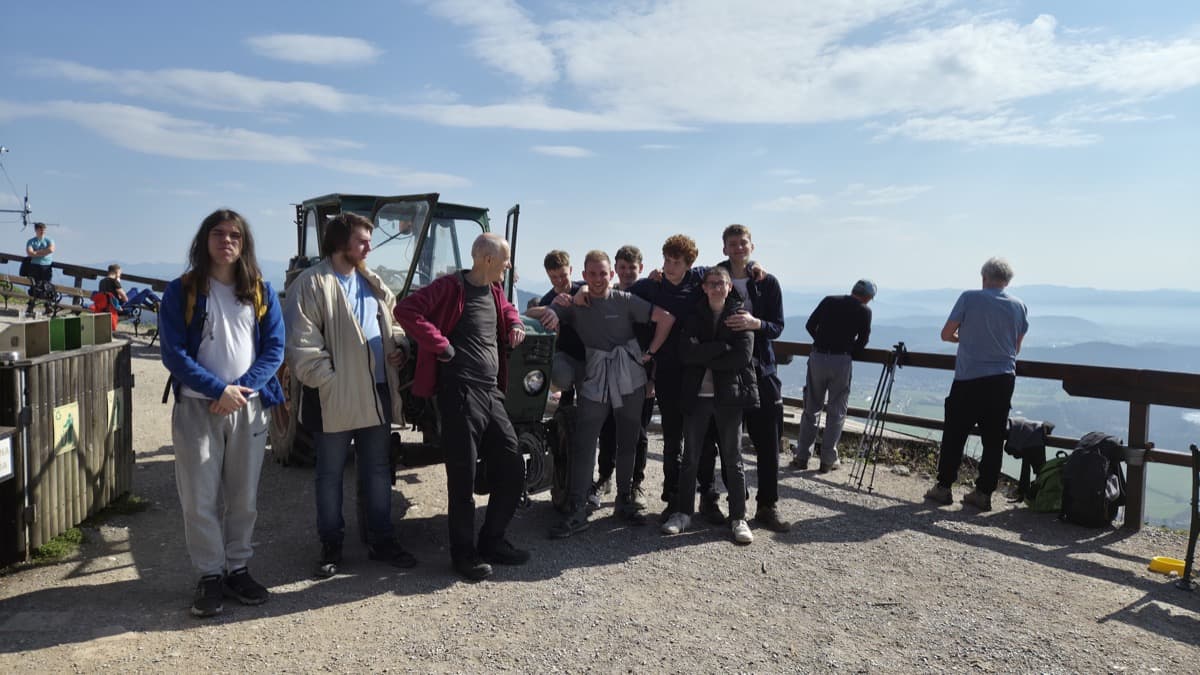 skupina dijakov na vrhu Šmarne gore, stojijo pred zelinm trakotorjem, v ozadju pogled na s soncem obsijano Ljubljansko kotlino